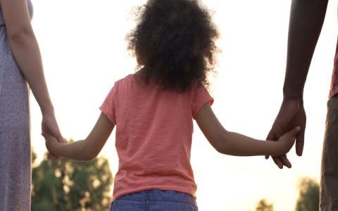 bambina di spalle tenuta per le mani da due adulti