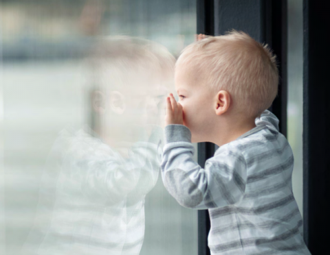 immagine di un bambino piccolo solo che guarda attraverso una vetrata