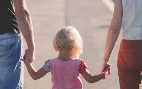 immagine di due adulti di spalle che conducono per mano una bambina