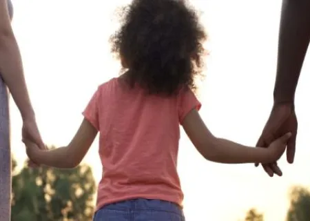 bambina di spalle tenuta per le mani da due adulti