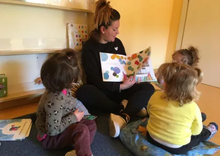 gruppo di persone con un adulto che legge un libro a tre bambini di spalle